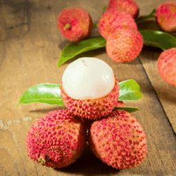 Fresh lychee fruit with red textured skin and juicy white flesh arranged on a wooden surface