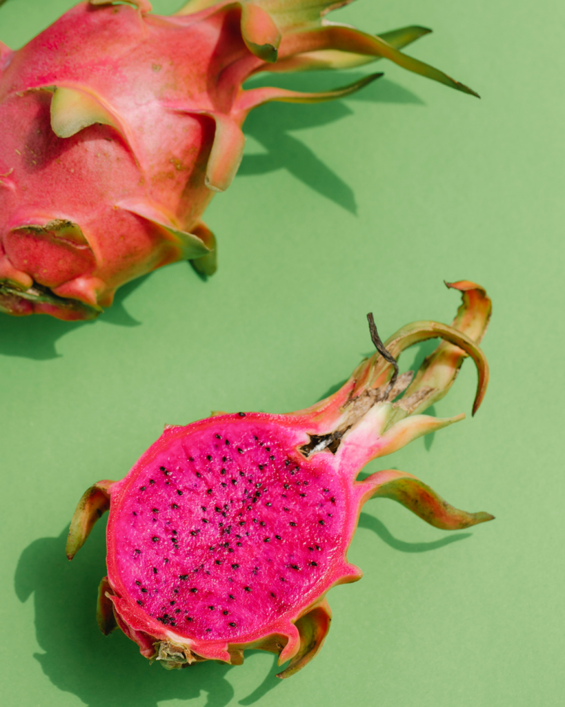 Halved red dragon fruit displaying rich, deep pink-purple flesh and bright green outer scales.