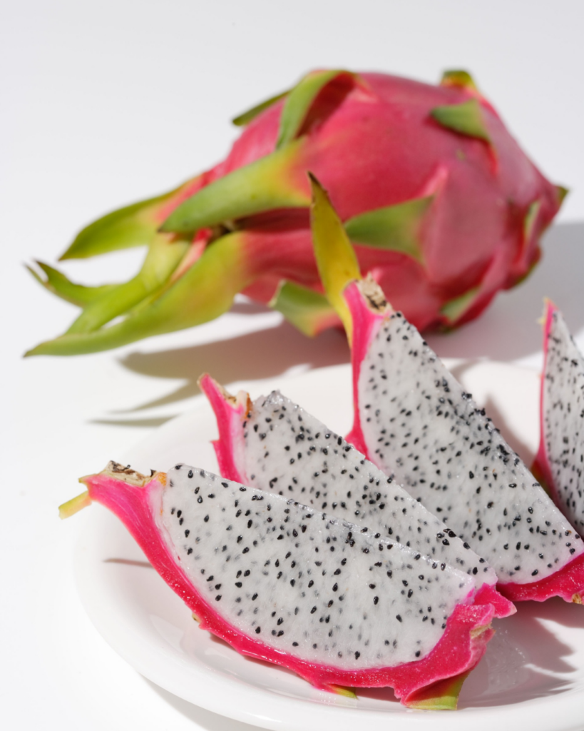 Whole and sliced white-flesh dragon fruit showing vibrant pink skin and white specked interior with black seeds.